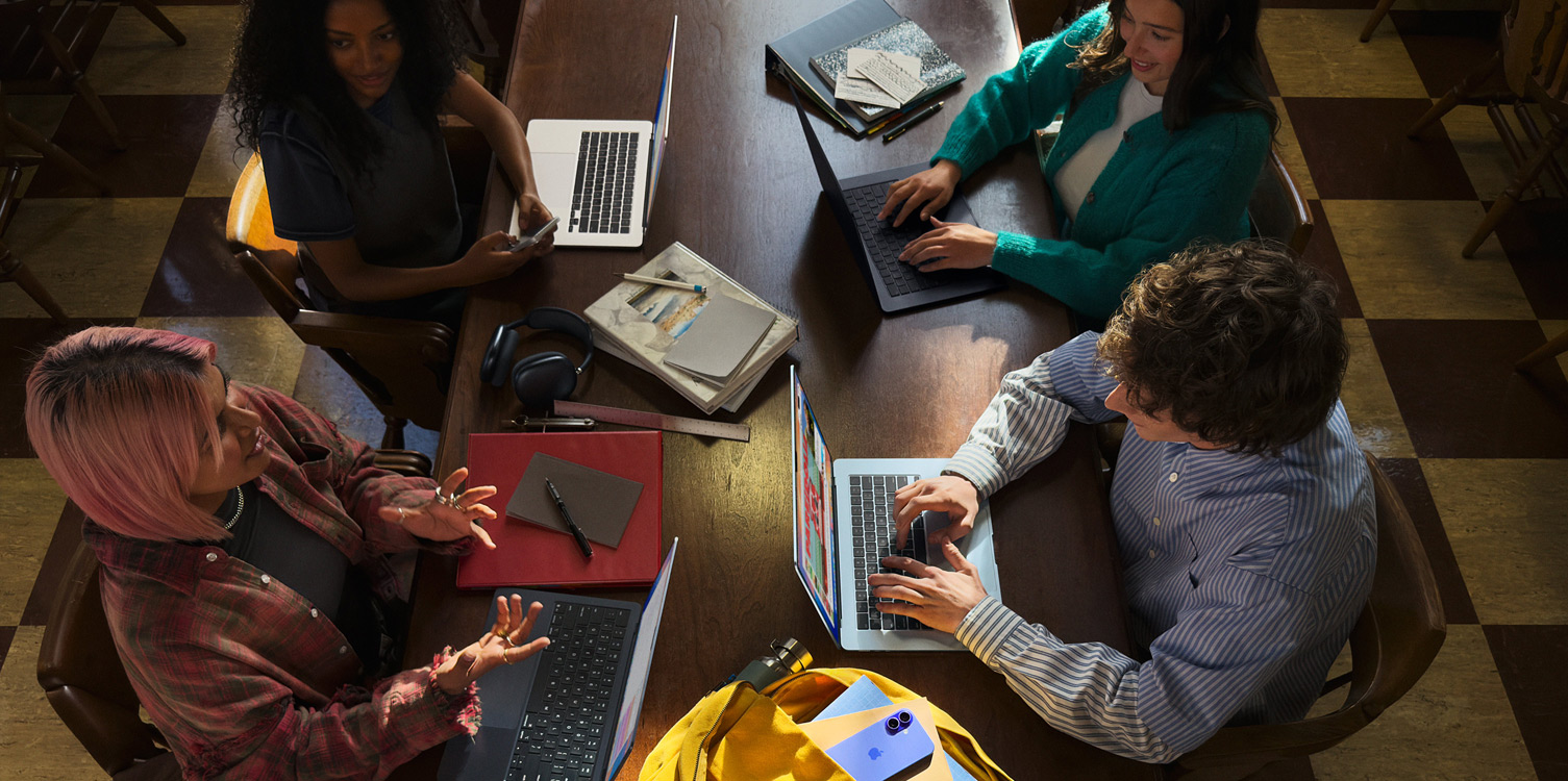 Four students sitting at a table. They have their MacBook computers and notes open in front of them.