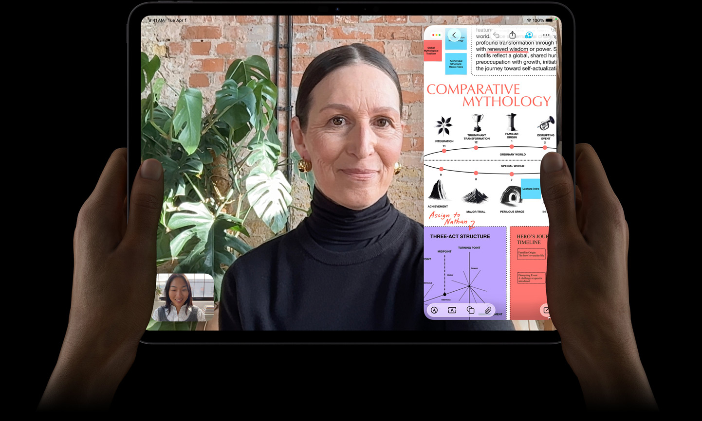 iPad Pro, etupuoli, tähtimusta väri, vasen ja oikea käsi pitelevät laitetta vaakasuunnassa, pyöristetyt kulmat, musta näytön kehys, näytöllä on FaceTime-keskustelu ja sen livekäännös sekä opetusappi, jossa on tekstiä, kaavioita ja käsinkirjoitettuja muistiinpanoja sisältävä esitelmä aiheesta ”Comparative Mythology”