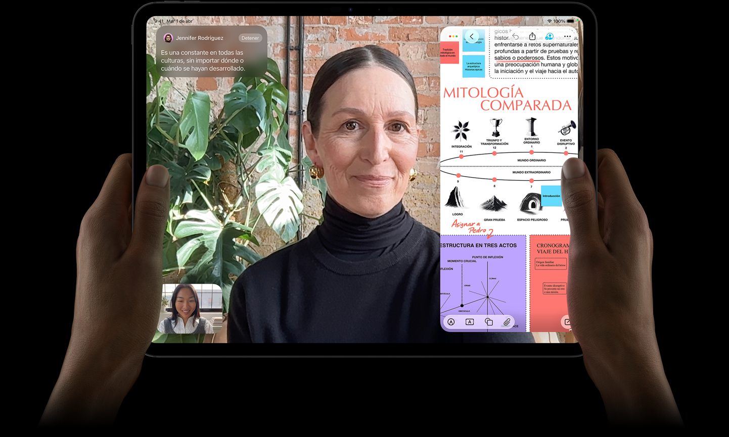 iPad Pro, parte frontal, color negro espacial, manos izquierda y derecha lo sostienen en posición horizontal, esquinas redondeadas, marco de la pantalla negro, la pantalla muestra una conversación en FaceTime que se está traduciendo en vivo, y una app educativa con una presentación sobre mitología comparada con texto, diagramas y notas escritas a mano