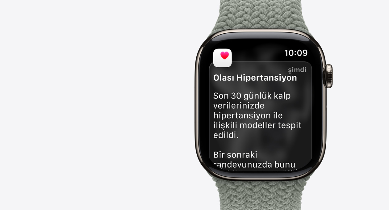 Apple&nbsp;Watch&nbsp;Series&nbsp;11, natürel renk, titanyum kasa, olası hipertansiyon bildirimi, beyaz kutu içinde pembe kalp, sağ dış görünüm, Digital&nbsp;Crown, kordon, yeşil gri renkte Örgü&nbsp;Solo&nbsp;Loop