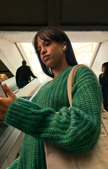 Ένα άτομο που φοράει AirPods Pro 3 κοιτάει το iPhone του