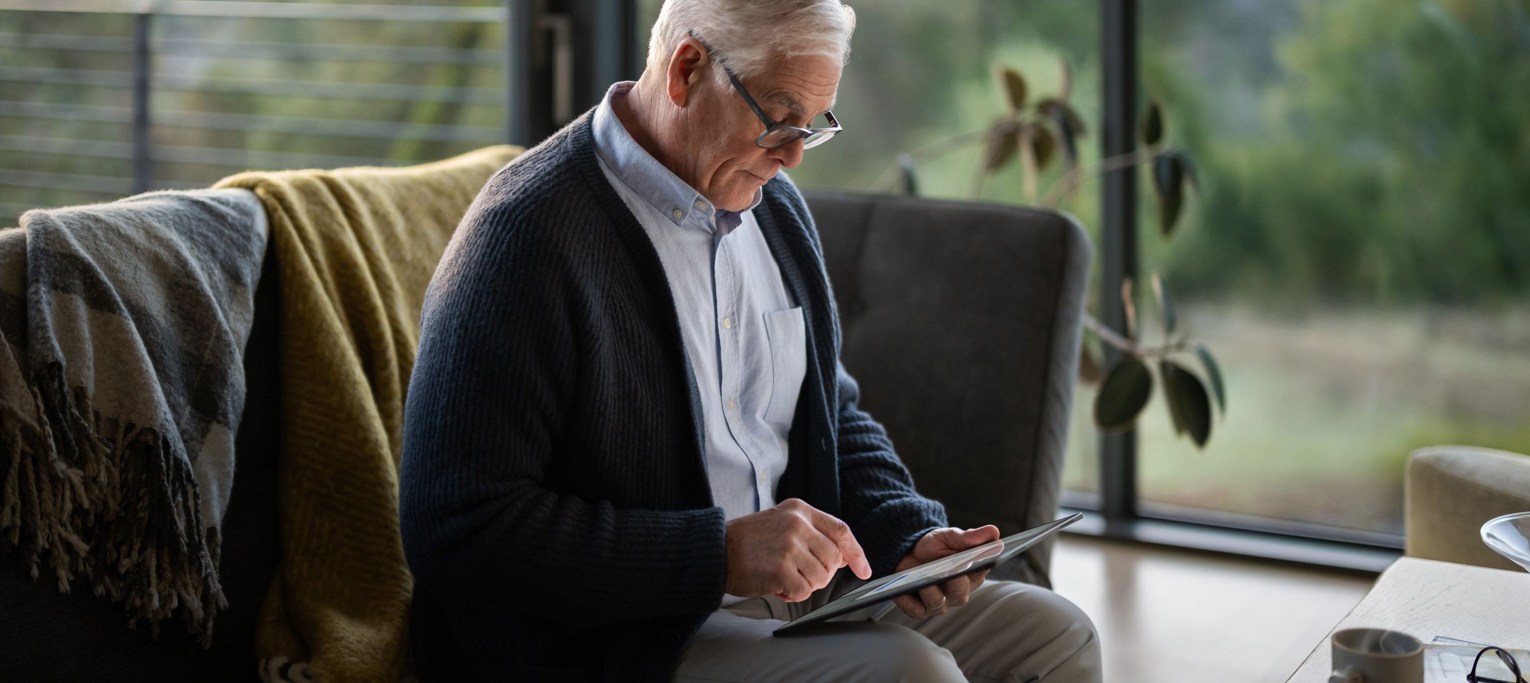Un homme âgé, assis sur un canapé, regarde un iPad.