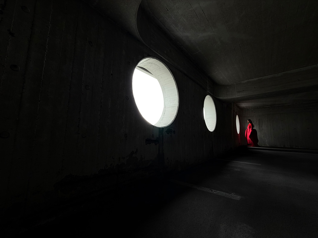 A woman wearing a long red dress stands in an empty room being photographed. The Photo app toggles through the focal lengths to demonstrate the capabilities of the pro camera system, showcasing: 13 mm