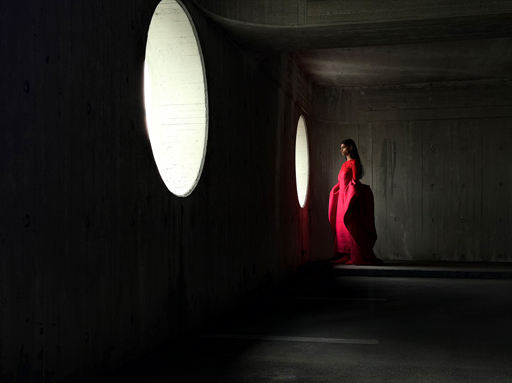 A woman wearing a long red dress stands in an empty room being photographed. The Photo app toggles through the focal lengths to demonstrate the capabilities of the pro camera system, showcasing: 48 mm